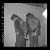 Two Hell's Angels motorcycle gang members in handcuffs, facing wall showing designs on back jackets in Los Angeles, Calif