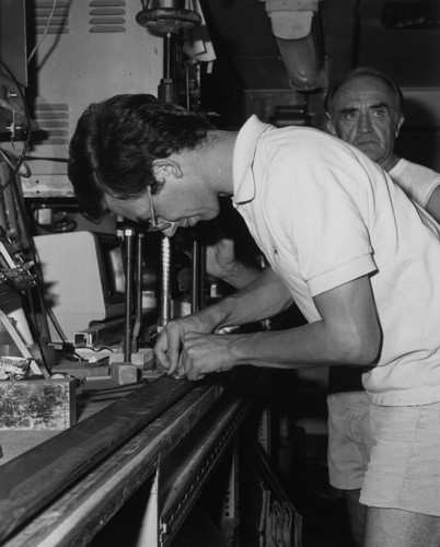 Scientist Andreas Wetzel and a unidentified man behind him on board the D/V Glomar Challenger (ship), Wetzel is sampling one of the cores taken during Leg 96 of the Deep Sea Drilling Project. 1983