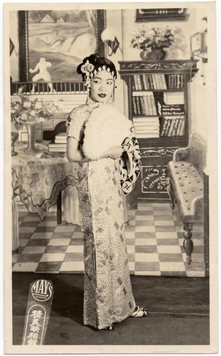 Actress dressed in floorlength cheongsam holds an ostrich fan and looks to the left /