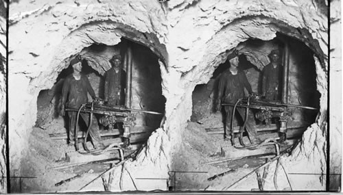 Miner drilling in copper mine with machine drill, undercutting, (this is the operation before blasting and caving. Caving ground can be seen to the rear. Probably Globe, Arizona