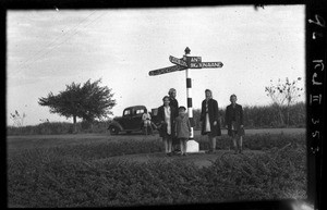 Women and children of European origin standing in front of a signpost, Xinavane, Mozambique, ca. 1940-1950