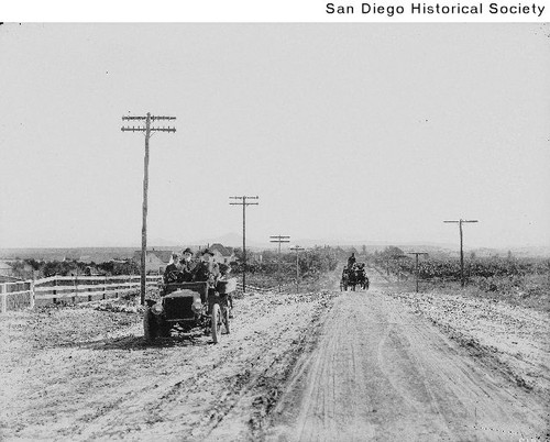 Automobile with three men on the side of the road with a team of horses approaching in the distance