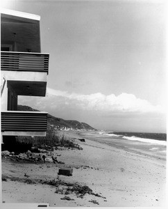 A view of a beach house right along the edge of the beach as waves rush in