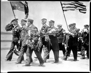 Veterans marching towards the ocean holding flowers during Memorial Day ceremonies, ca.1925-1930