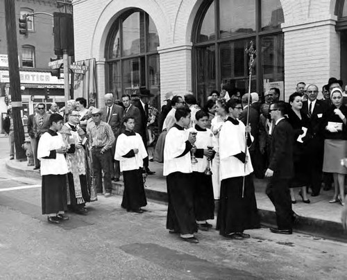 Priest and altar boys walking in front of the Simpson building holding candles and crucifix