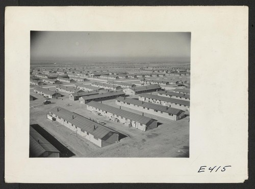Overlooking the Amache Relocation Center, near Granada, Colorado. In the foreground is a typical barracks unit consisting of 12 six room apartment barracks buildings, a recreation hall, laundry and bathrooms, and the mess hall. Photographer: Parker, Tom Amache, Colorado