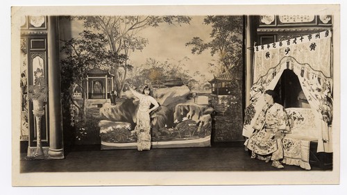 Woman dances for a man seated on a bed /