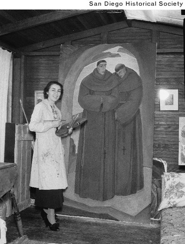 Artist Belle Baranceanu standing with a painting of two monks