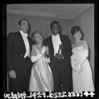 Sidney Poitier holding his Oscar pose with Gregory Peck, Annabella and Anne Bancroft backstage at the Academy Awards, Los Angeles, 1964