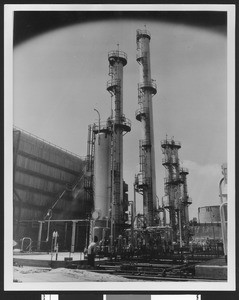 Exterior view of an unidentified oil refinery, showing a cluster of towers, ca.1940