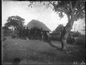 African people in front of a building with a thatched roof, Antioka, Mozambique, ca. 1916-1930