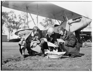Three aviators examining a document in front of an airplane