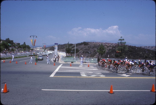 [1984 Olympics Men's Cycling Road Race with pack of cyclists approaching intersection slide]