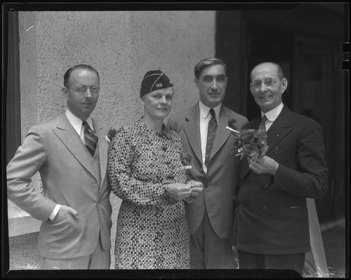 Three men and one woman posing with flowers and military-style hat, 1936