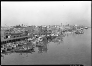 View of Fish Harbor showing boats docked to piers with canneries in the background, San Pedro, February 10, 1928