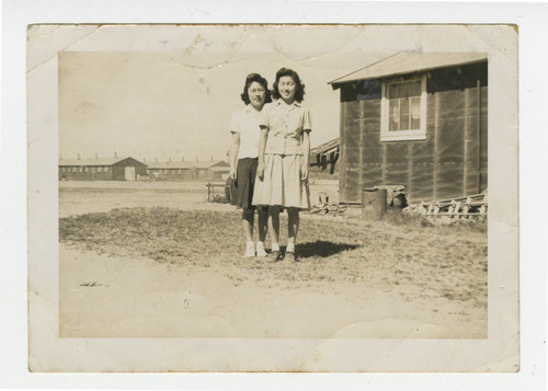 Nisei women standing outside with barracks in the background