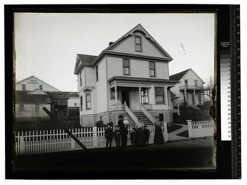 [Family posing in front of two story home; Pioneer Stables in background]