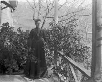 Woman posing on porch, orchard in background, c. 1912
