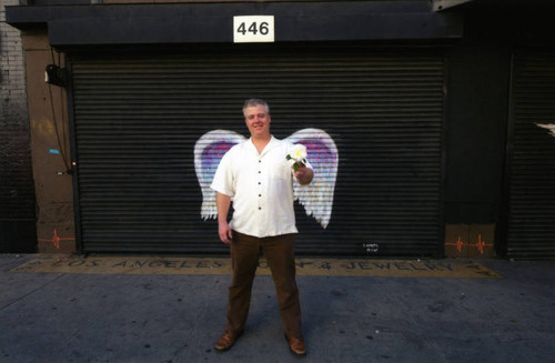 Unidentified man holding a white flower posing in front of a mural depicting angel wings