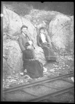 Two women and a man pose near railroad track