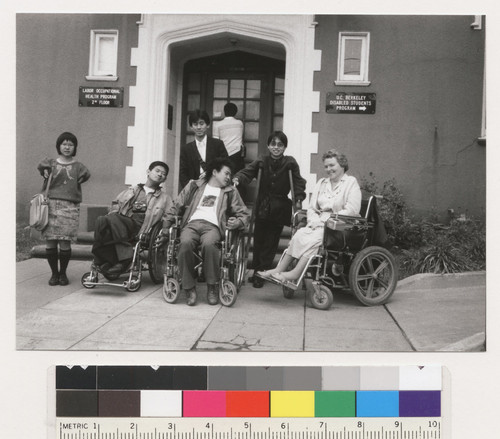 Unidentified people posing and Susan O'Hara in front of the U.C. Berkeley Disabled Students Program building, three are in wheelchairs, one is on crutches and two are standing