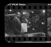 Tom Bradley holds sign for Freedom of Press exhibit while at reception for the event with Otis Chandler and Hugh Hefner. A. 1980