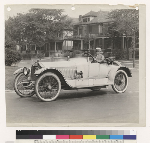 Doble in driver's seat of a model in front of houses, side view