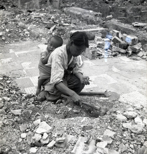 Woman with a baby on her back sifting through rubble