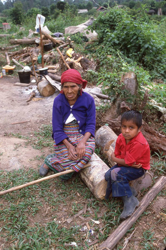 An older woman and a child sit on logs at a refugee camp, Chajul, ca. 1983