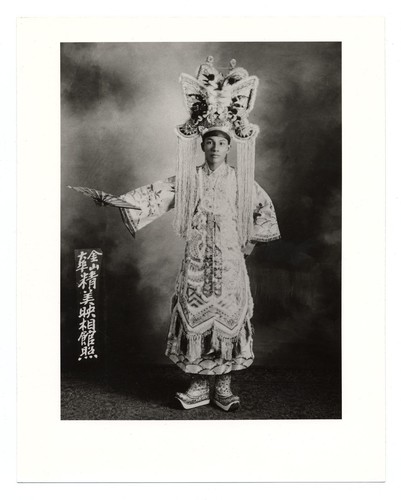 Portrait of an actor in the role of scholar gallant in classical costume, elaborate headdress and platform boots, holding a folding fan /