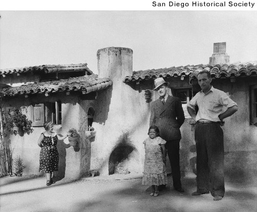 Two men with two midget women standing outside a building in the Midget Village during the 1935 Exposition