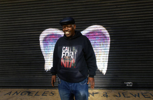 Unidentified man in a cap and sweatshirt posing in front of a mural depicting angel wings