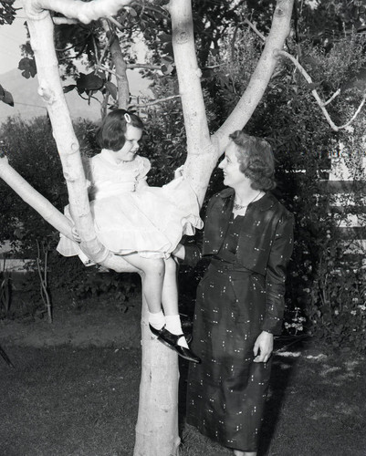 Girl sits in a tree with a woman standing next to her