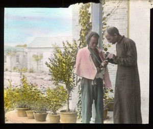 Fr. Anthony Cotta, MM, examining a man's hand, China, ca. 1906-1919