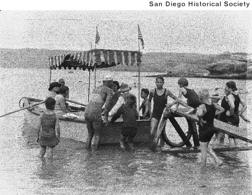People wading in the water at La Jolla Cove, guiding a rowboat to a gangplank