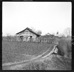 View of a farm house and vegetable garden, showing a small child, China, ca.1900