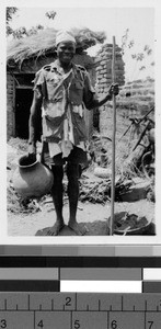 Man holding a stick and pot by a brick wall, Africa, January 1948