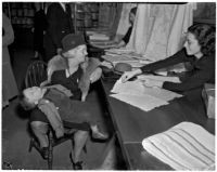 Mrs. Henry Clark looks at fabrics displayed by clerk Lee Maler as baby Warren Hancock sleeps in her lap, Los Angeles, 1925-1945