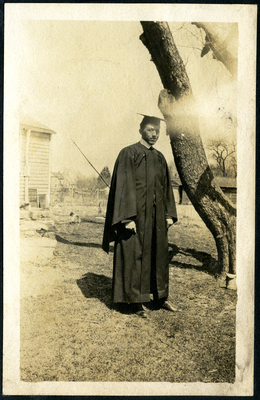 Man in cap and gown standing next to tree