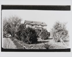 Unidentified two-story Queen Anne Victorian home with ornate fretwork and a small orchard, 1940s or 1950s