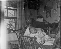 Baby in wicker carriage indoors, c. 1912