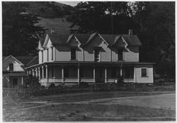 Unidentified two-story, Queen Anne Victorian farm house with a wrap-around porch, located below a grass- and chaparral-covered hillside in western Sonoma County, 1960s or 1970s