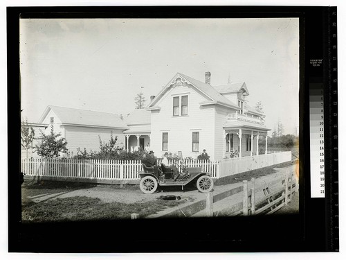 [Three people sitting in an automobile parked beside a house]