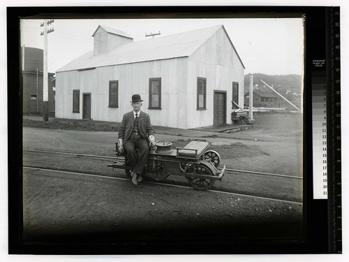 [Well dressed man sitting on railroad scotter car]