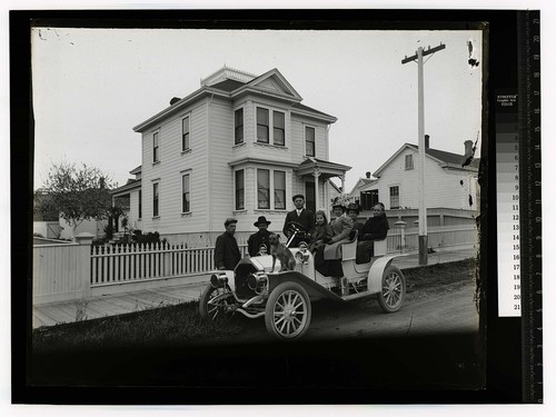 [Family and dog pose in an open auto on a residential street]