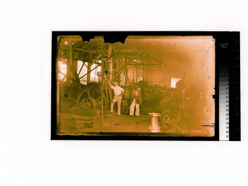 [Two men pose in an industrial shop]