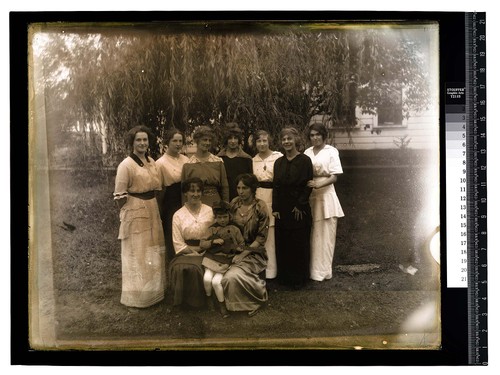 [Nine women and one girl pose under a willow tree]