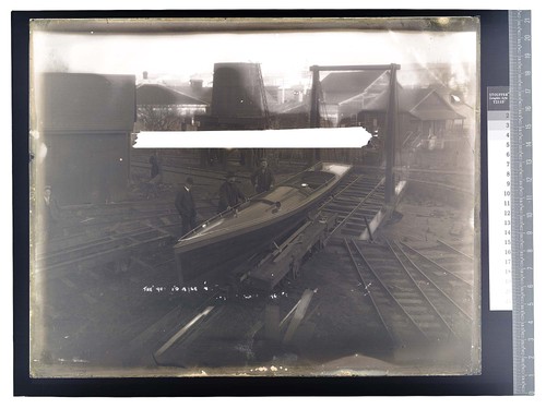 [Three men gathered by side of small boat in an industrial setting]