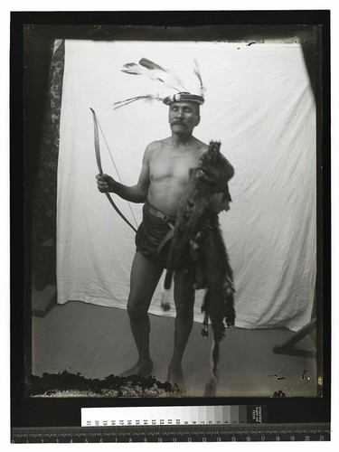 [Portrait of an Indian man with ceremonial headdress standing in front of a drape]