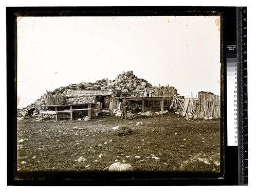 [Rustic building of stone and wood with man standing in doorway, another man nearby]